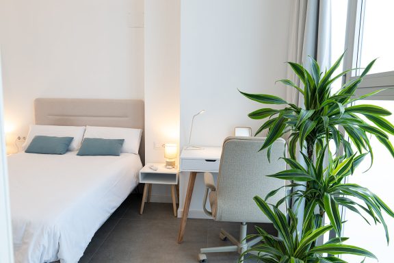 Dormitorio moderno con cama, lámparas, planta y escritorio.