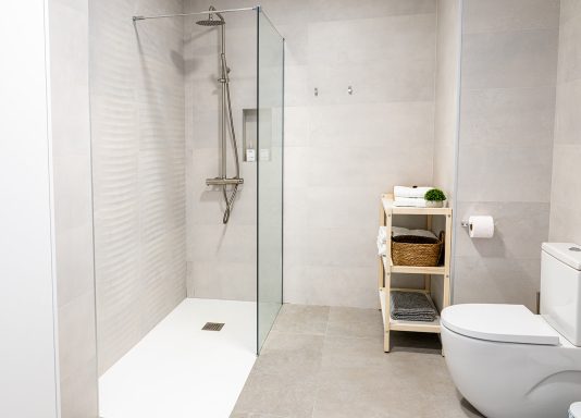 Baño moderno con ducha de cristal, inodoro y estantería de madera.