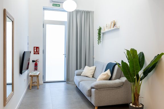 Sala de estar moderna con sofá, planta, espejo y ventana con cortinas.