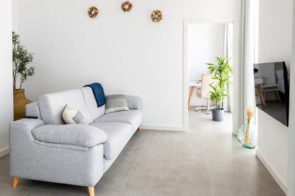 Sala de estar minimalista con sofá gris, planta y pared blanca.