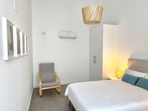 Habitación luminosa con cama, silla de madera y decoración minimalista.