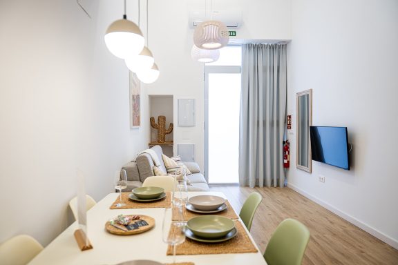 Comedor moderno con mesa, platos dispuestos y luz natural entrando por la ventana.